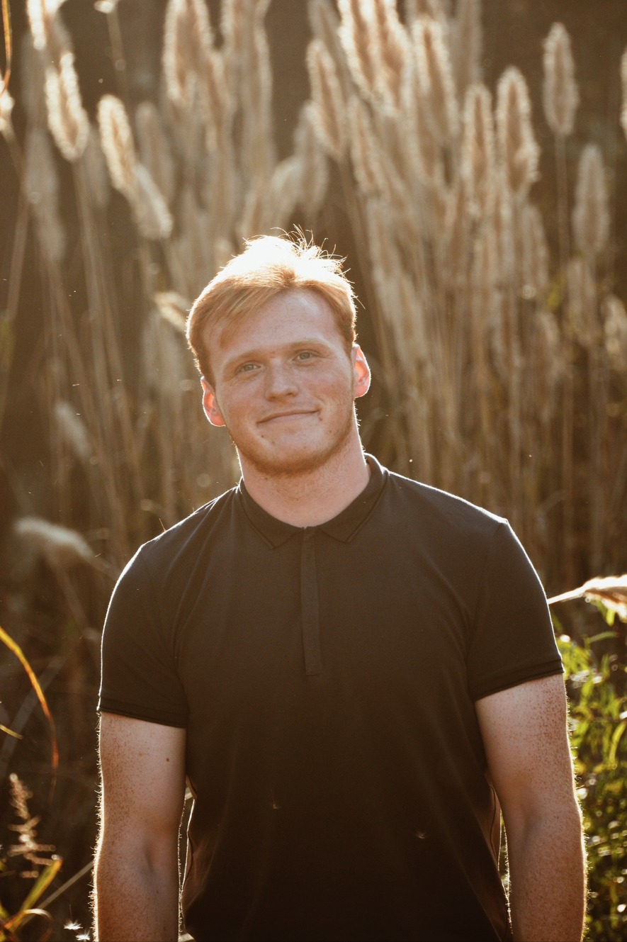 Young man in a black polo at sunset in tall grasses