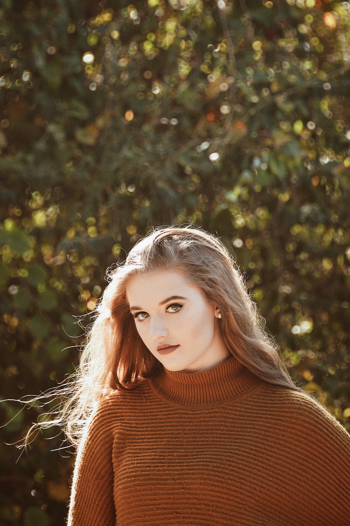 Backlit portrait of a young woman in a rust turtleneck sweater