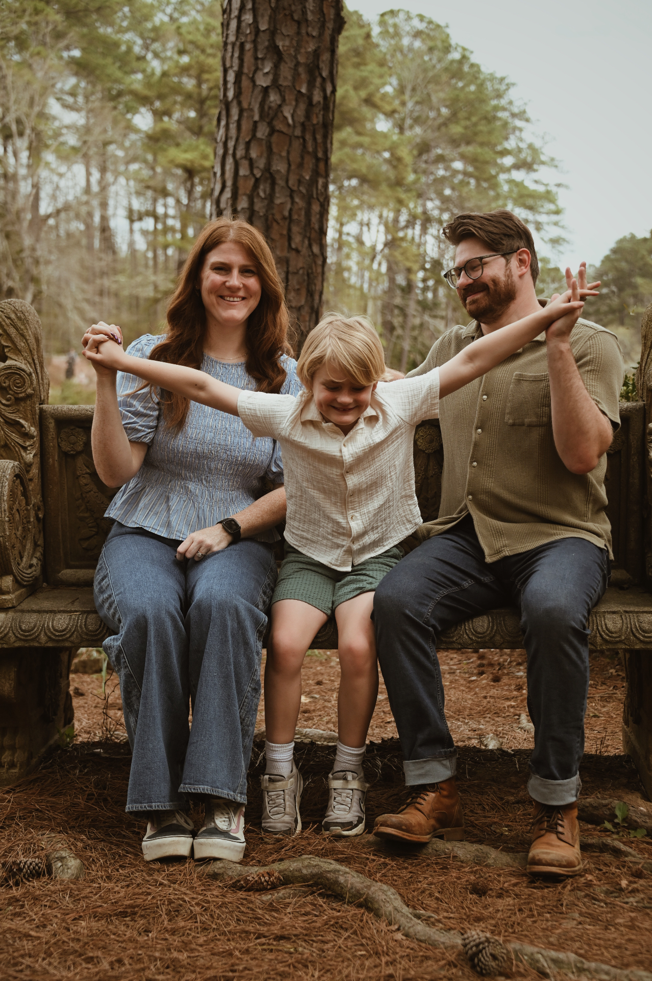 Family of three holding hands while sitting on a carved bench