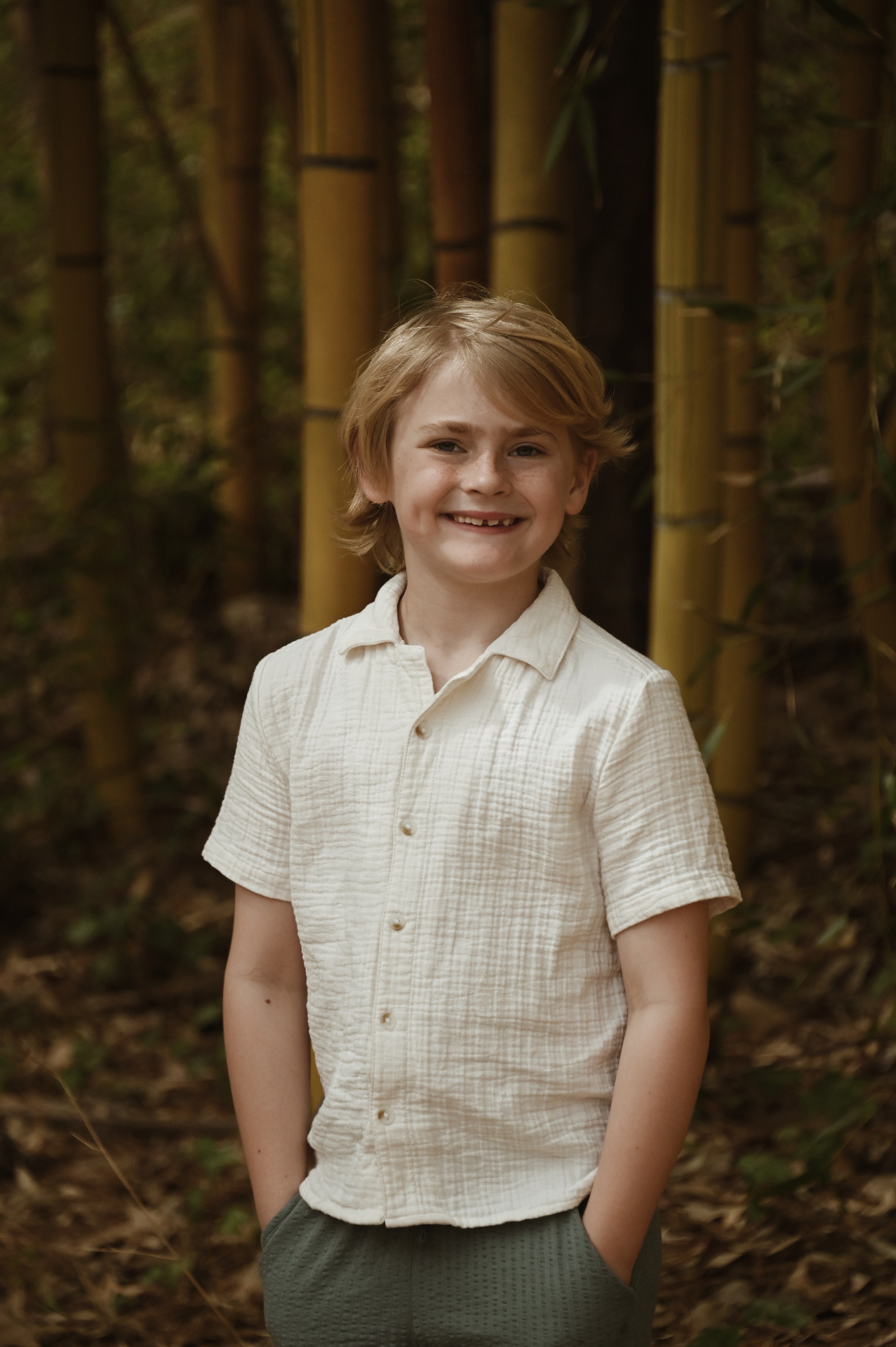 Young boy in a linen shirt smiling in a bamboo grove