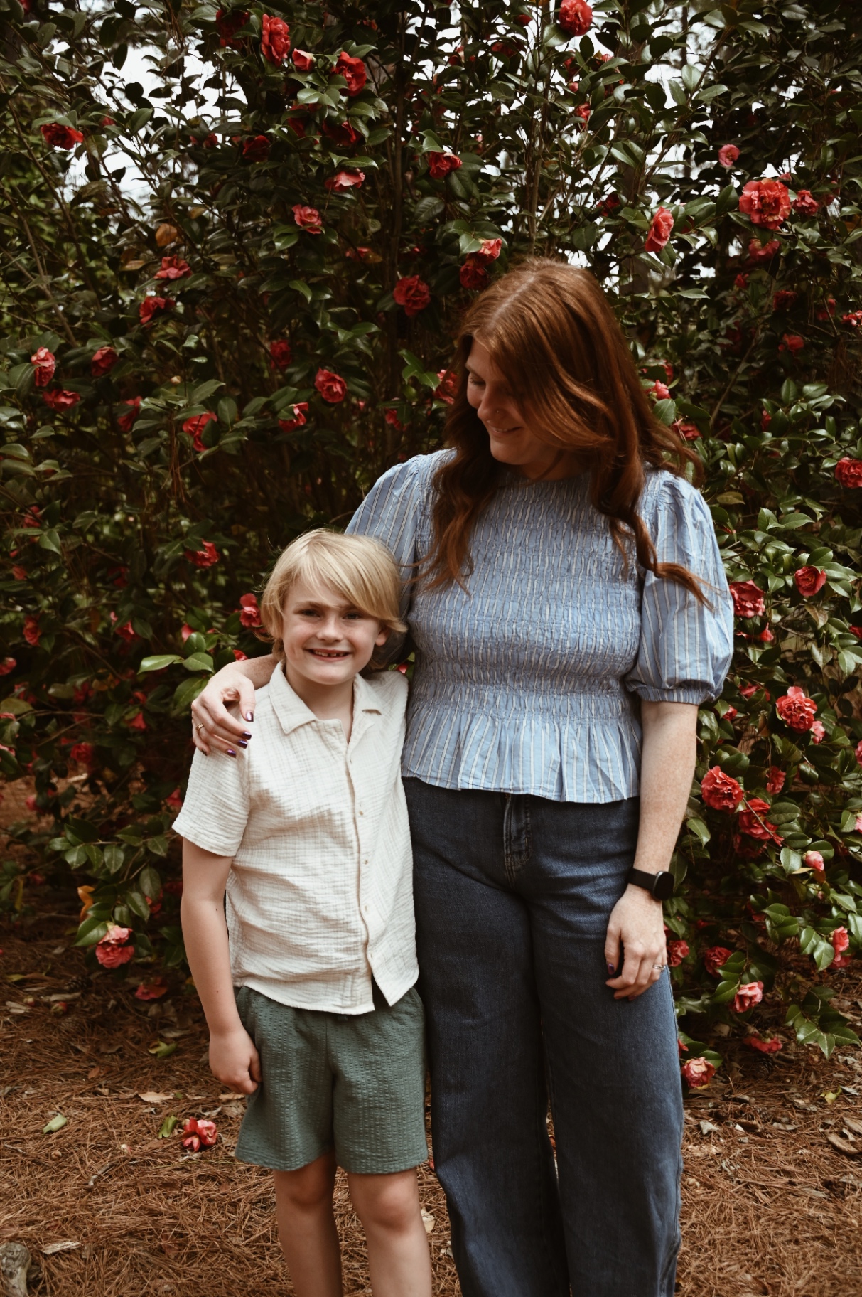 Mother and son smiling together in front of red camellia flowers