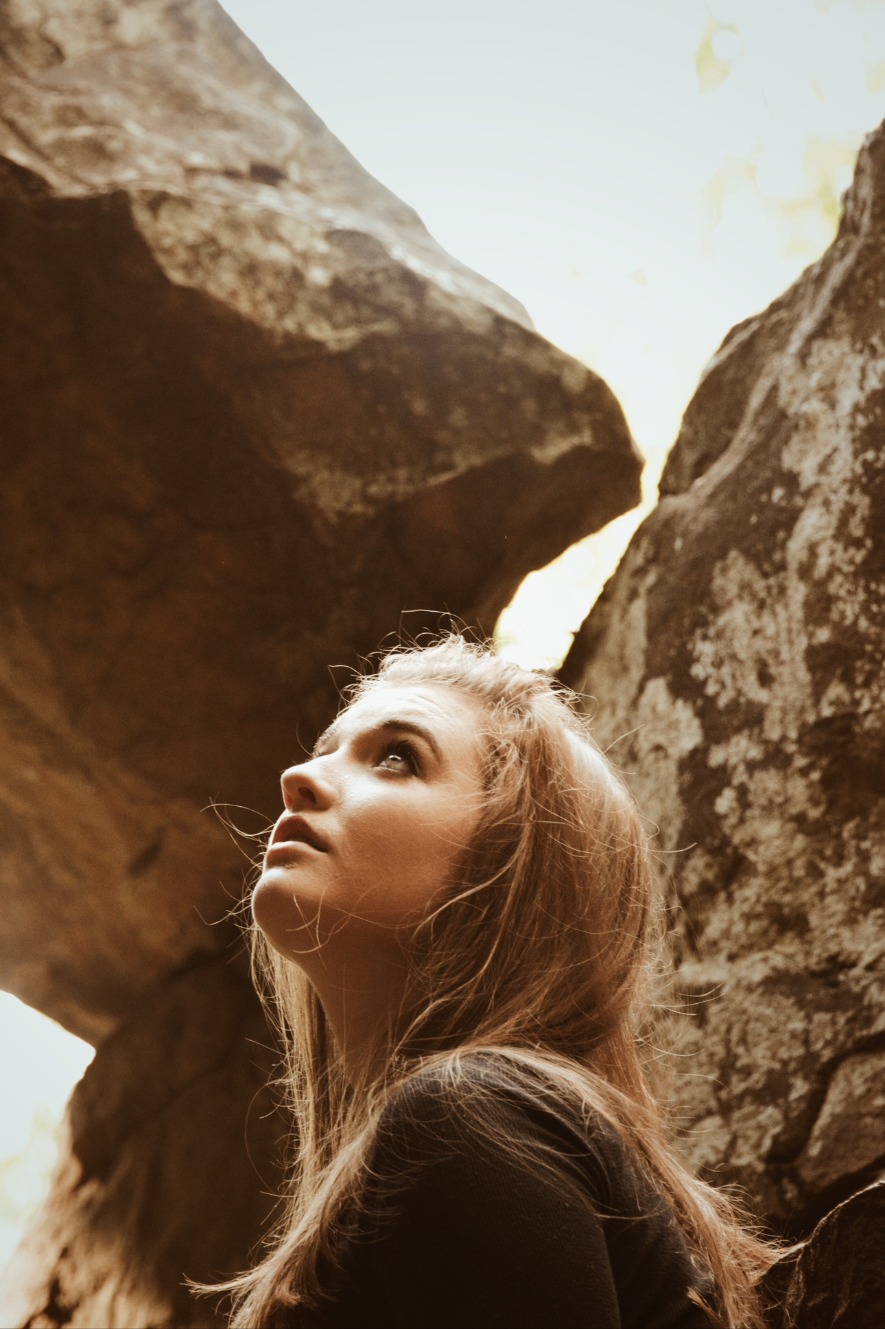 Portrait of a young woman gazing upward between large rocks