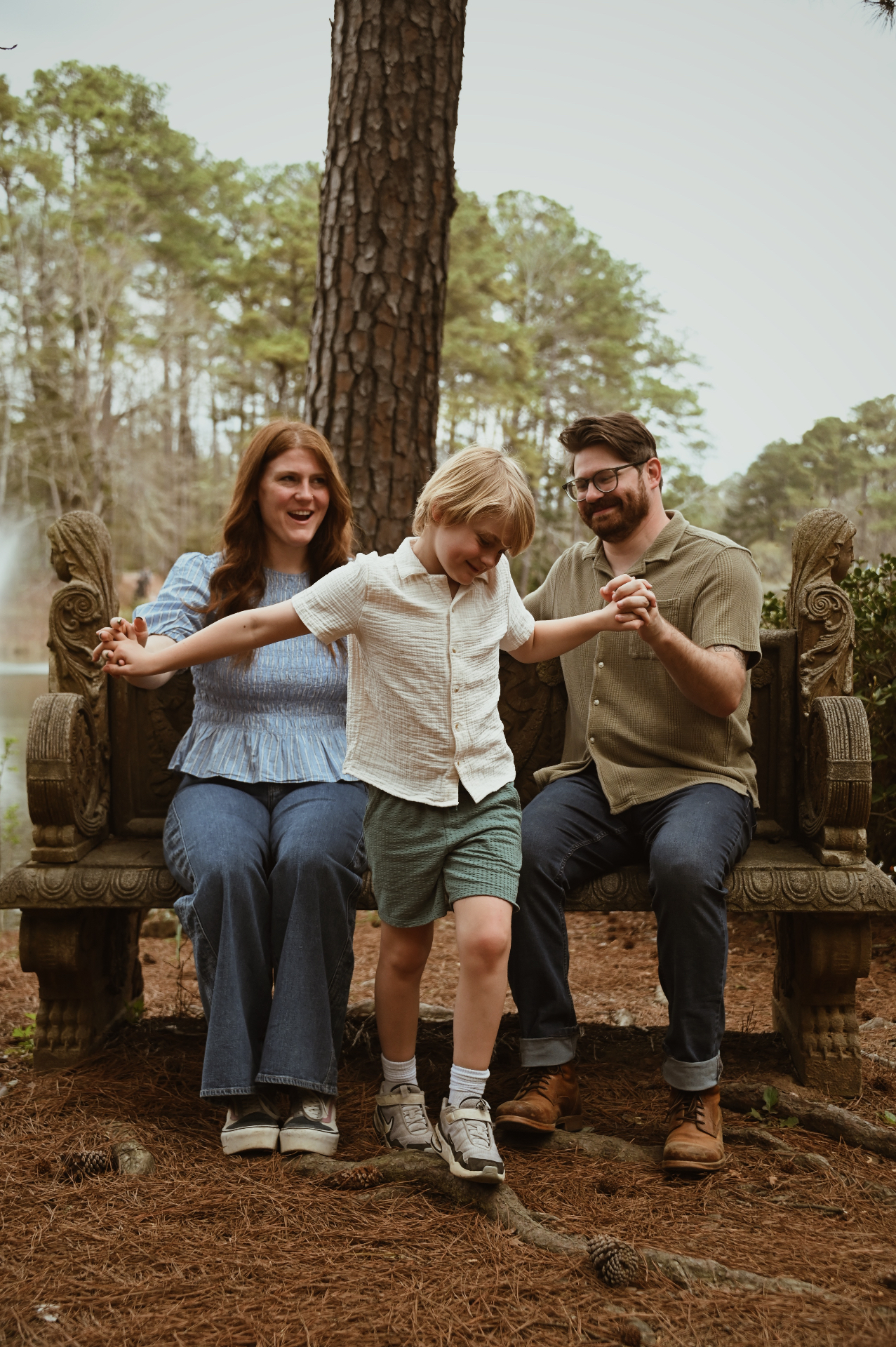 Young boy jumping while holding parents' hands on a stone bench