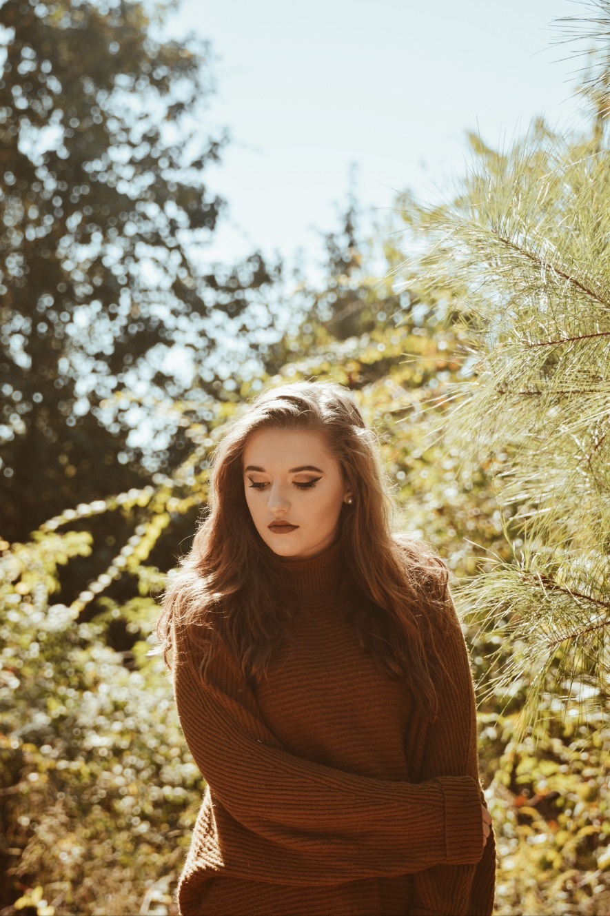 Young woman in a rust sweater looking down in soft light