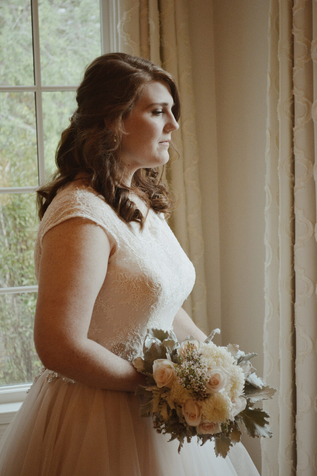 Bride in lace gown holding a bouquet of pale roses