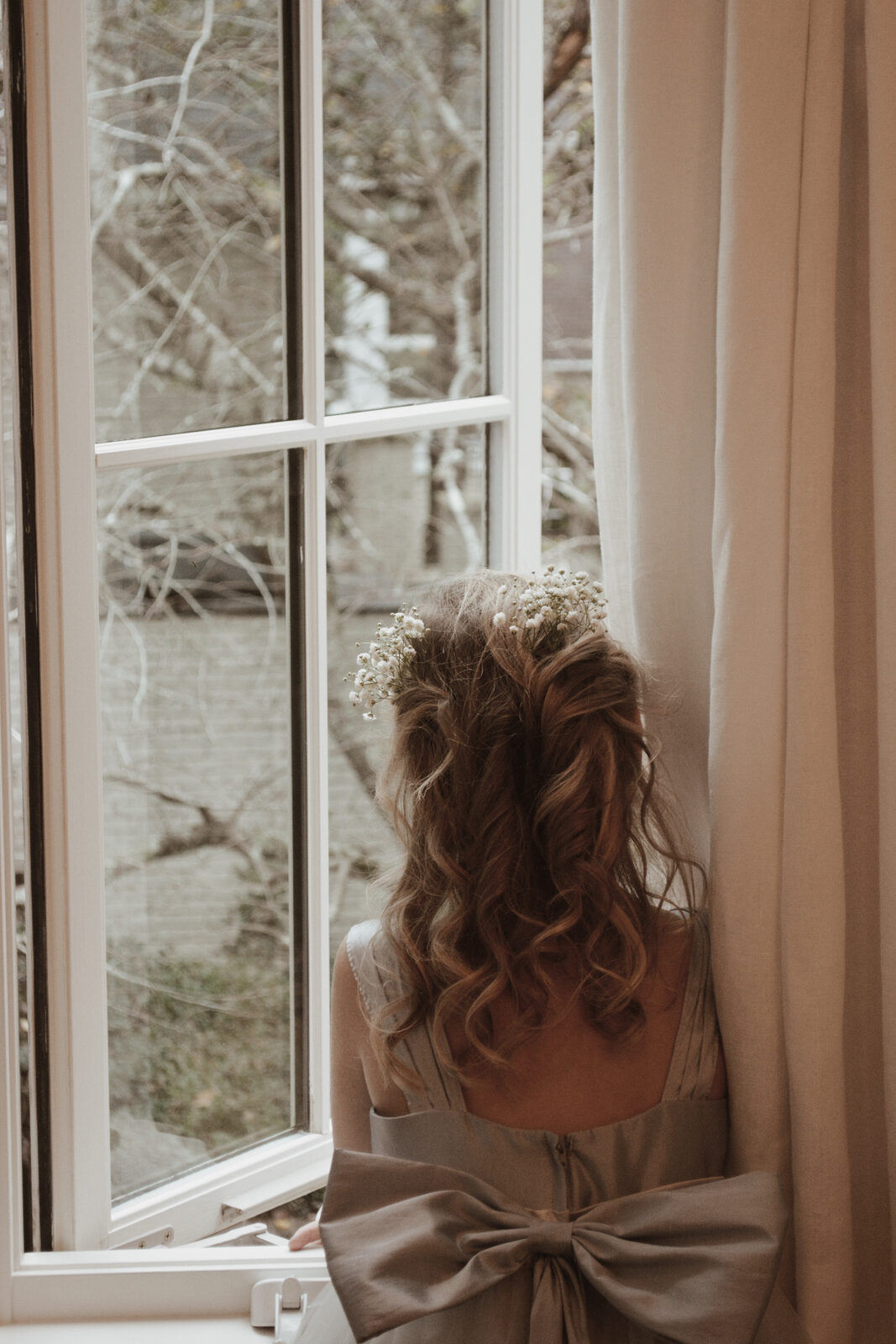 Bridesmaid with baby's breath in her hair by a window