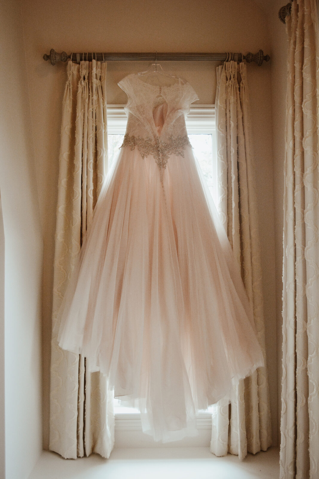 Blush wedding gown hanging in a window